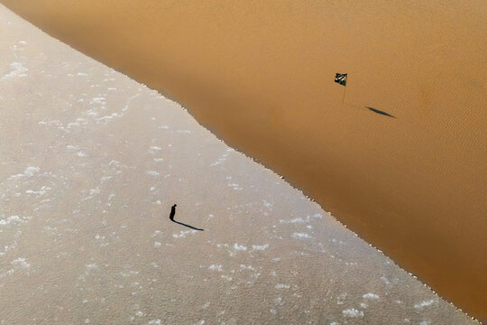 Aerial view of a lone person standing on a salt flat next to a sand dune with a small flag planted in the sand in Al-Faw, Basra Governorate, Iraq.