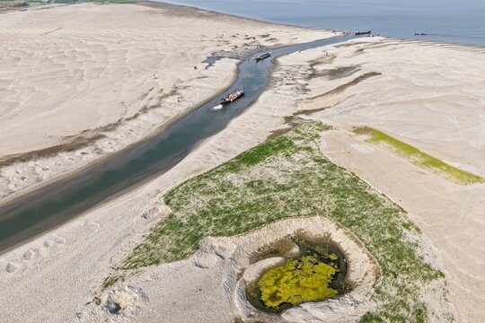 Aerial view of a winding river flowing through a vast sandy landscape with small boats navigating the channel and patches of green vegetation in Gaibandha, Rangpur Division, Bangladesh.