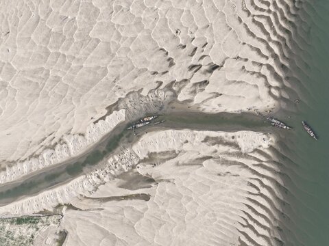 Aerial view of the intricate sandbars and river channels of the Brahmaputra River with small traditional boats navigating the water in Gaibandha, Rangpur Division, Bangladesh.