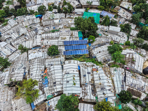 Cox's Bazar, Bangladesh - 17 July 2026: Aerial view of a dense refugee camp with makeshift shelters, white tarpaulins, solar panels on roofs, and scattered trees.