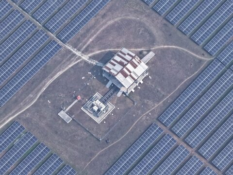 Aerial view of a solar power plant with rows of photovoltaic panels surrounding a central maintenance building and electrical substation in Gaibandha, Rangpur Division, Bangladesh.