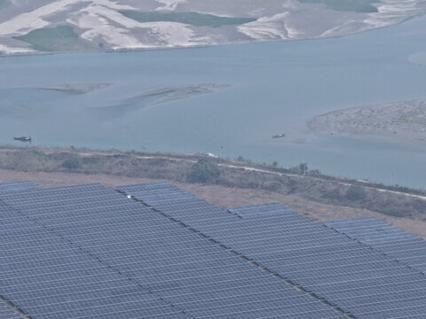 Aerial view of a large solar power plant with rows of photovoltaic panels situated near a riverbank with small boats in Gaibandha, Rangpur Division, Bangladesh.