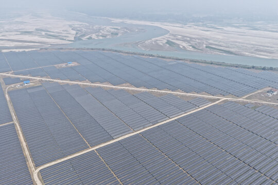 Aerial view of a large solar power plant with rows of photovoltaic panels, dirt access roads, and a river in the background in Gaibandha, Rangpur Division, Bangladesh.