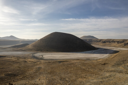 Aerial view of Lake Meke, a volcanic crater lake with a central cinder cone surrounded by arid landscape and dry salt flats under a soft sky in Karapinar, Konya, Turkiye.