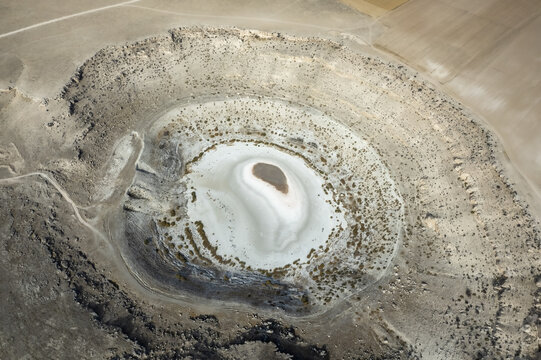 Aerial view of Meyil Lake, a natural sinkhole with white mineral deposits surrounded by arid terrain and agricultural fields in Karapinar, Konya, Turkiye.