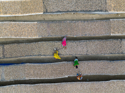 Cox's Bazar, Bangladesh - 11 March 2026: Aerial view of workers drying fish on large mats in the sun, with colorful clothing contrasting against the textured surface.