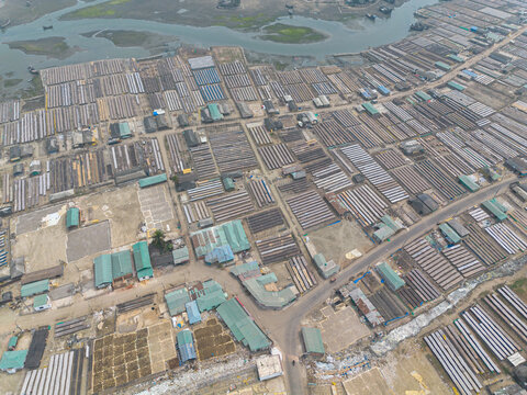 Aerial view of extensive fish drying racks with rows of rectangular beds and small buildings with green roofs near the river in Cox's Bazar, Chittagong Division, Bangladesh.