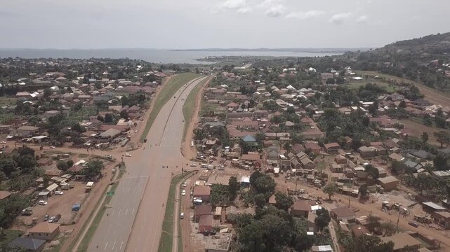 Aerial view of the Kampala Northern Bypass Highway winding through residential neighborhoods with distant lake views under an overcast sky in Kampala, Central Region, Uganda.