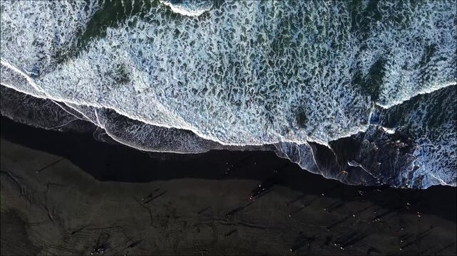 Aerial view of Parangtritis Beach with dark volcanic sand and crashing ocean waves in Kretek, Special Region of Yogyakarta, Indonesia.