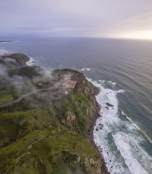 Aerial view of the lighthouse at Cape Roca surrounded by dramatic cliffs, green coastal landscape, and mist over the Atlantic Ocean in Colares, Lisboa, Portugal.