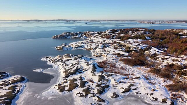 Aerial view of Stora Amundon featuring snow-covered rocky terrain and icy coastal waters in Hovas, Vastra Gotalands lan, Sweden.