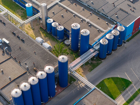 Aerial view of raw milk storage and cooling tanks at a dairy processing facility with industrial piping and rooftops in Suwalki, Podlaskie Voivodeship, Poland.
