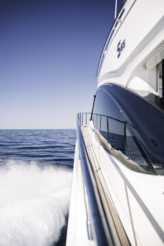 Balearic Islands, Spain - 20 April 2024: View of a modern yacht cruising the Mediterranean Sea off Mallorca, with a sleek white hull, teak deck, and blue water wake under a clear sky.