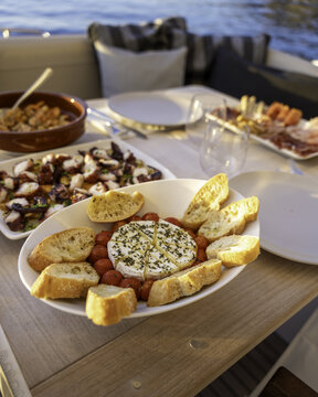 Balearic Islands, Spain - 20 April 2024: View of a delicious spread of tapas including octopus, baked camembert with cherry tomatoes and crusty bread served on a boat table in Mallorca.