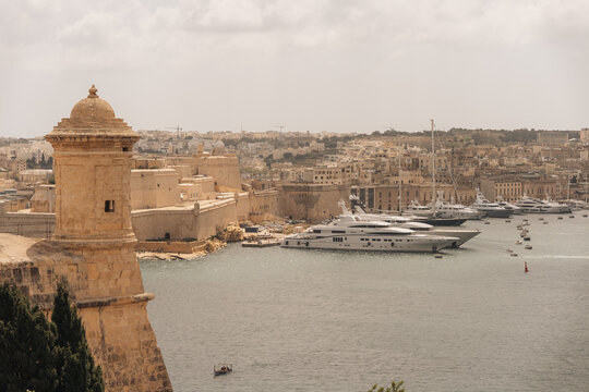 Valletta, Malta - 15 July 2022: View of Fort St. Angelo and luxury yachts docked in the Grand Harbour, with historic limestone fortifications and the cityscape of Valletta under a cloudy sky.