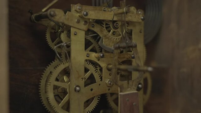 Side view macro shot of layered brass gears, cogs, and wheels spinning inside the internal mechanical movement of a vintage antique grandfather clock.