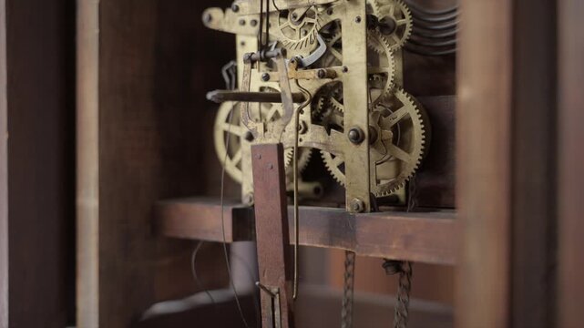 Close up shot of a person pulling a heavy brass weight chain to wind the mechanical gears and internal clockwork of an old antique grandfather clock.