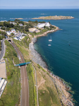 Aerial view of the Dalkey coastline featuring the railway line entering a tunnel, coastal cliffs, Dalkey Island, and boats in the Irish Sea near Dublin, County Dublin, Ireland.