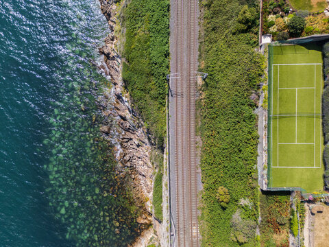 Aerial view of the Dalkey coastline featuring a railway track running alongside the sea and a tennis court situated on the cliffside in Dublin, County Dublin, Ireland.