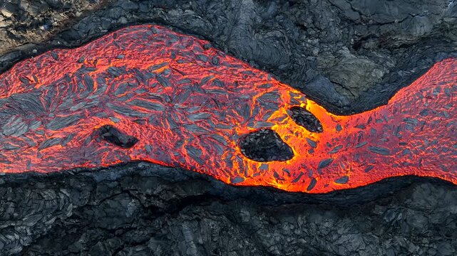 Aerial view of Litli-Hrutur volcanic eruption with glowing molten lava flowing over dark solidified volcanic rock in Grindavik, Grindavikurbaer, Iceland.