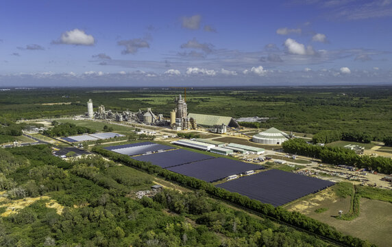 Aerial view of the Cemento Panam industrial facility with a large solar panel array and manufacturing buildings set in the green landscape of Los Llanos, San Pedro de Macoris, Dominican Republic.