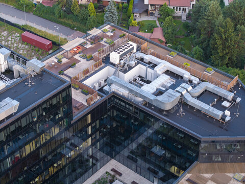Aerial view of a modern office building rooftop featuring extensive HVAC ventilation systems, a landscaped terrace with seating areas, and glass facades in Krakow, Lesser Poland Voivodeship, Poland.