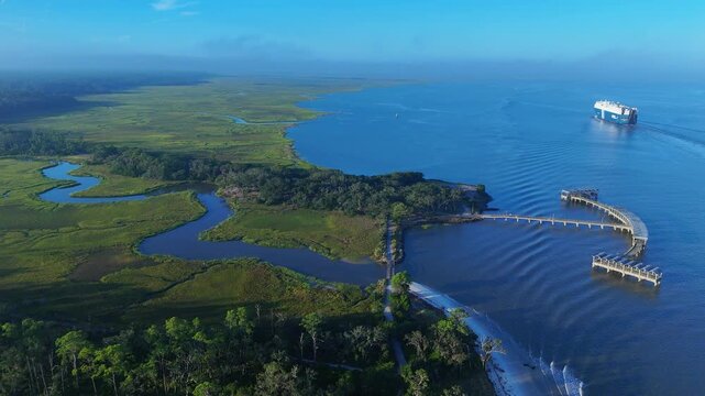 Aerial view of the salt marshes and pier at Jekyll Island with a cargo ship sailing in the Atlantic Ocean, Jekyll Island, Georgia, United States.