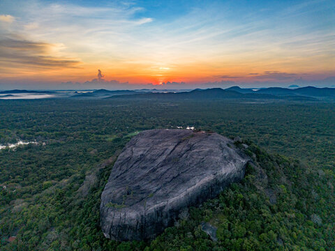 Aerial view of Pidurangala Rock surrounded by lush green forest under a vibrant sunset sky in Sigiriya, Central Province, Sri Lanka.