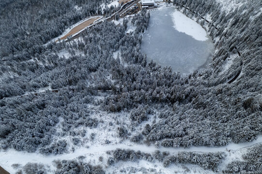 Aerial view of the frozen Mummelsee lake surrounded by a dense snow-covered pine forest in the Black Forest region of Seebach, Baden-Wurttemberg, Germany.