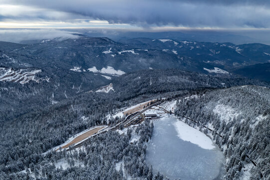 Aerial view of the frozen Mummelsee surrounded by snow-covered pine forests and mountains in the Black Forest in Seebach, Baden-Wurttemberg, Germany.