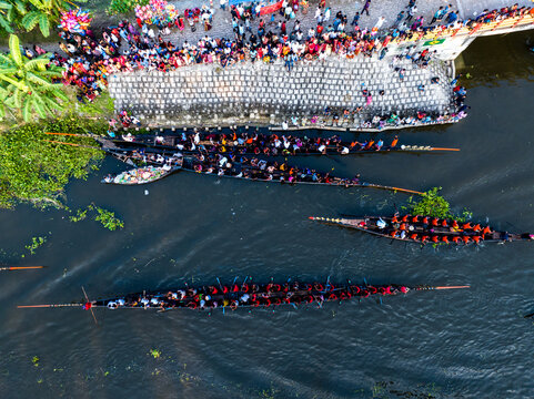 Gopalganj, Dhaka Division, Bangladesh - 30 October 2023: Aerial view of a traditional boat race with long wooden boats filled with rowers on a river, with crowds of spectators on the bank.