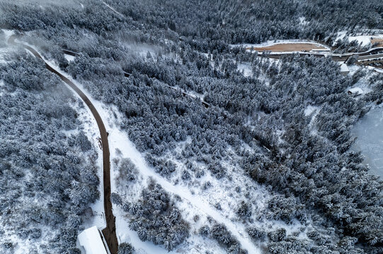 Aerial view of Mummelsee surrounded by a dense snow-covered forest and a winding road in Seebach, Baden-Wurttemberg, Germany.