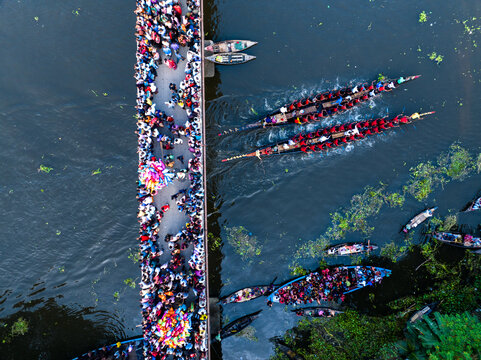 Gopalganj, Bangladesh - 30 October 2023: Aerial view of a crowded bridge filled with people watching a traditional boat race on the river, with long wooden boats navigating the water.