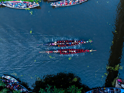 Gopalganj, Dhaka Division, Bangladesh - 30 October 2023: Aerial view of traditional boat racing with rowers in red shirts paddling long narrow boats on the river.