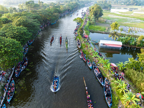 Gopalganj, Dhaka Division, Bangladesh - 30 October 2023: Aerial view of a traditional boat race on a canal, with long boats filled with people and spectators lining the lush riverbanks.