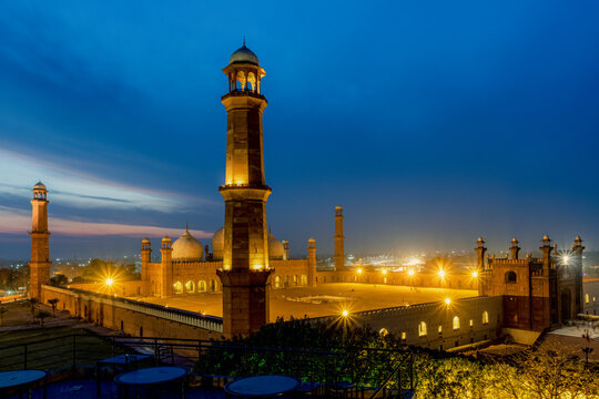 View of Badshahi Mosque at night with its illuminated minarets and domes glowing against a deep blue twilight sky in Lahore, Punjab, Pakistan.