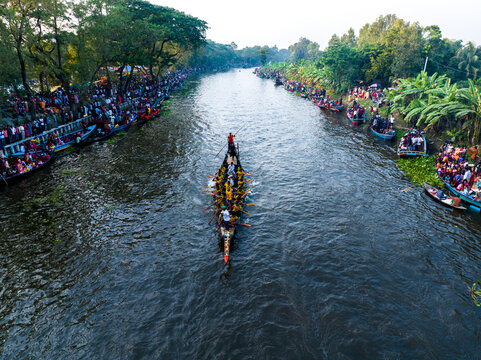 Gopalganj, Bangladesh - 30 October 2023: Aerial view of a traditional boat race on a river with rowers in long boats and crowds of spectators watching from the lush riverbanks.