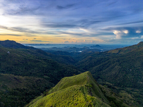Aerial view of Little Adam's Peak surrounded by lush green mountains and rolling hills under a dramatic sunset sky in Badulla, Uva Province, Sri Lanka.