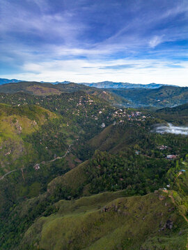 Aerial view of Little Adam's Peak surrounded by lush green mountains, rolling hills, and dense forests under a blue sky in Badulla, Uva Province, Sri Lanka.