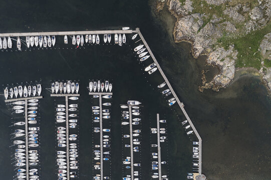 Aerial view of Sando marina with numerous sailboats docked in parallel rows along wooden piers, surrounded by rocky coastline and dark water in Vallda, Hallands lan, Sweden.