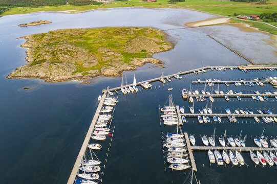 Aerial view of Sando marina with numerous sailboats docked in rows along wooden piers, surrounded by calm blue water and green coastal landscape in Vallda, Hallands lan, Sweden.