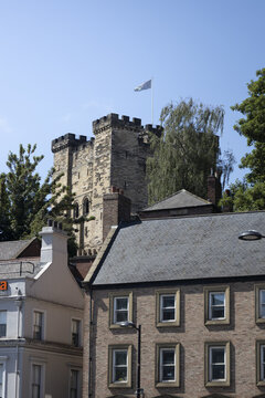 View of the historic Newcastle Castle keep with a flag flying against a clear blue sky, rising above traditional brick buildings in Newcastle upon Tyne, England, United Kingdom.
