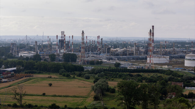 Aerial view of the industrial refinery complex featuring tall chimneys, storage tanks, and intricate pipe networks surrounded by green fields in Gdansk, Pomeranian Voivodeship, Poland.