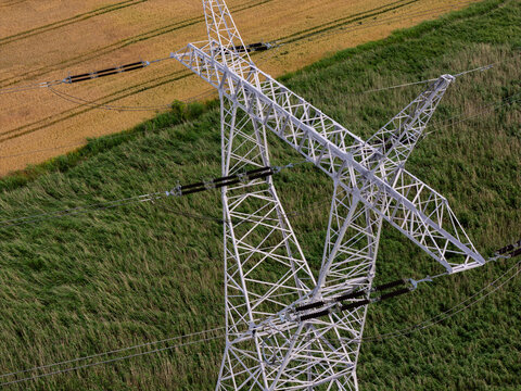 Aerial view of a high-voltage power line pylon standing amidst green fields and golden crops in Gdansk, Pomeranian Voivodeship, Poland.