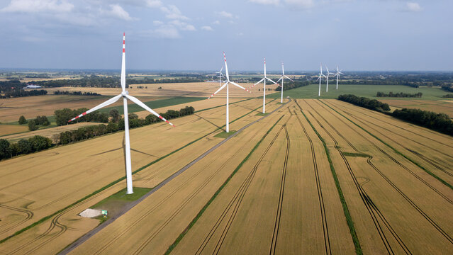 Aerial view of wind turbines standing in a vast golden wheat field under a clear blue sky in Gdansk, Pomeranian Voivodeship, Poland.