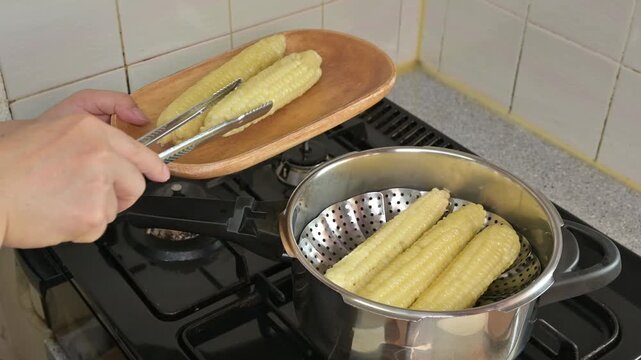 집게로 냄비에서 갓 찐 옥수수를 건져 올리는 모습