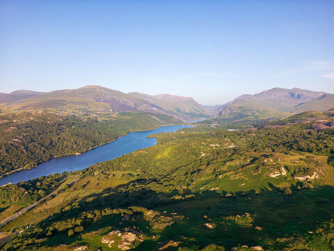 Aerial view of Llyn Padarn surrounded by lush green mountains and rolling hills in the Snowdonia region of Cwm-y-glo, Wales, United Kingdom.