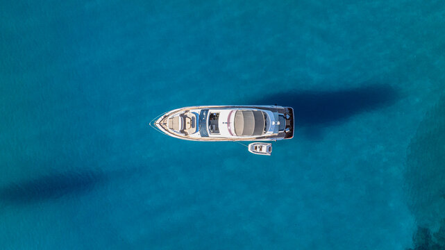 Balearic Islands, Spain - 20 April 2024: Aerial view of a luxury motor yacht with a small tender boat anchored in the clear turquoise waters off the coast of Mallorca.