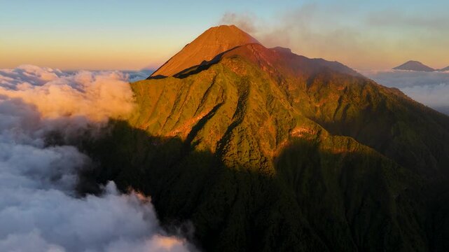 Aerial view of Merapi volcano at sunrise with lush green slopes and clouds in Cepogo, Central Java, Indonesia.