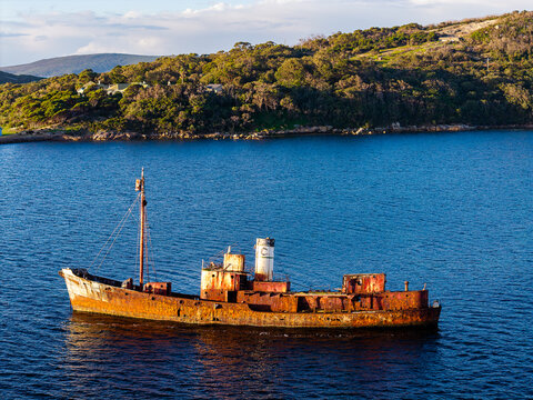 Aerial view of a rusty shipwreck floating in the deep blue water near the forested coastline of the Vancouver Peninsula, Western Australia, Australia.